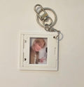 A white square photo ID holder keychain with a silver metal clasp and key ring, holding a printed photo of a smiling blonde person, shown against a plain off-white background.
